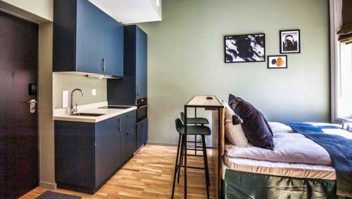 Hybelleilighet med moderne mørkt kjøkken og en seng med hodegavl