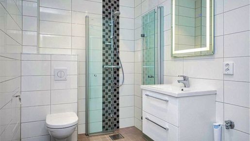 Lyst bad med hvite fliser, moderne baderomsinnredning, dusjvegger i glass og vegghengt toalett